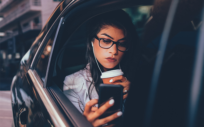 Woman sitting in a car listening to music looking at her phone with a cup in her hand
