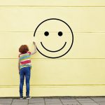 Girl drawing smiley face on to a wall.